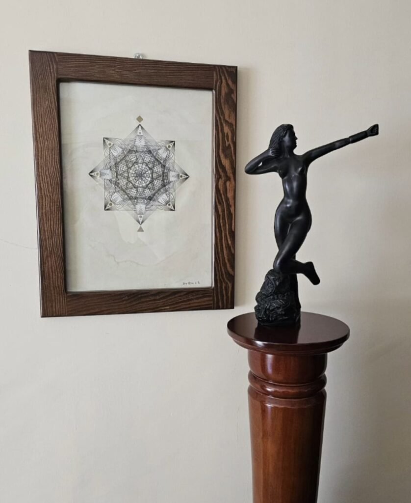 Cuadro de geometría en tinta en pared con fonso color netro y una escultura en bronce que decoran un espacio de cliente.